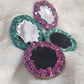Four epoxy resin pieces with crystal texture edges, two green and two purple, with black centers.