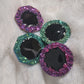 Four epoxy resin pieces with crystal texture edges, two green and two purple, with black centers.