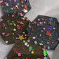Close up of hexagon shaped epoxy resin pieces filled with assorted glitter shapes and silver or gold holographic bases.