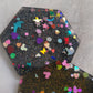 Close up of hexagon shaped epoxy resin pieces filled with assorted glitter shapes and silver or gold holographic bases.