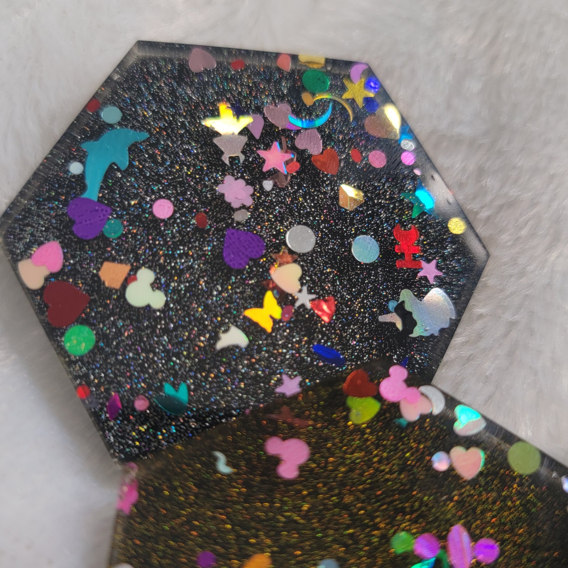 Close up of hexagon shaped epoxy resin pieces filled with assorted glitter shapes and silver or gold holographic bases.
