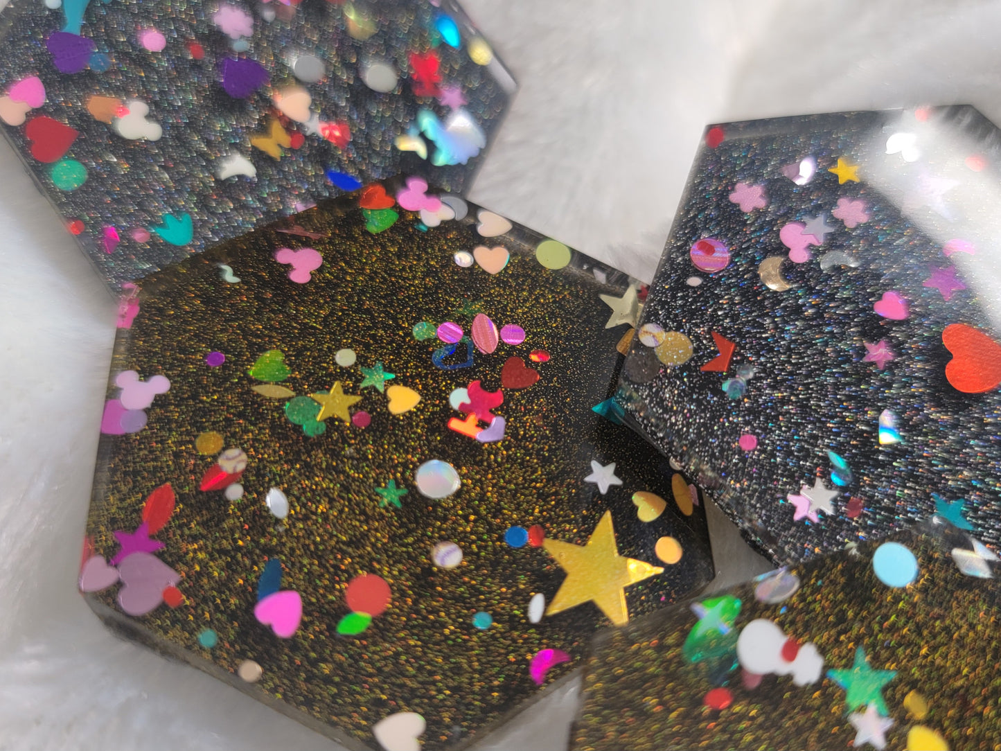 Close up of hexagon shaped epoxy resin pieces filled with assorted glitter shapes and silver or gold holographic bases.