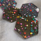 Close up of hexagon shaped epoxy resin pieces filled with assorted glitter shapes and silver or gold holographic bases.