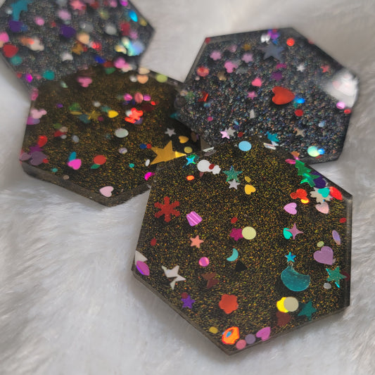 Close up of hexagon shaped epoxy resin pieces filled with assorted glitter shapes and silver or gold holographic bases.