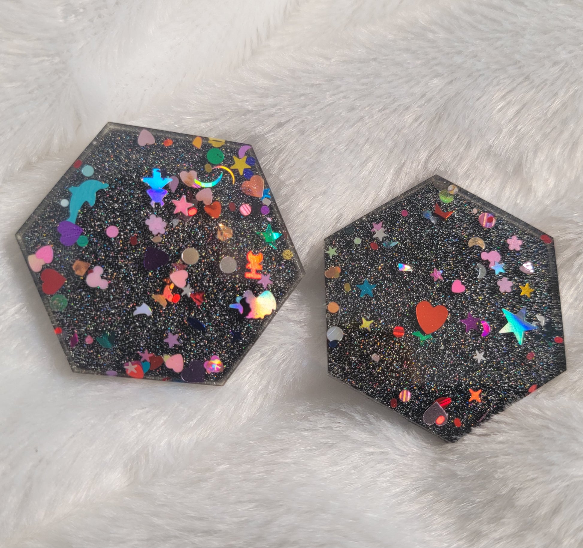 Two hexagon shaped epoxy resin pieces filled with assorted glitter shapes and a silver holographic base.