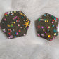 Two hexagon shaped epoxy resin pieces filled with assorted glitter shapes and a gold holographic base.