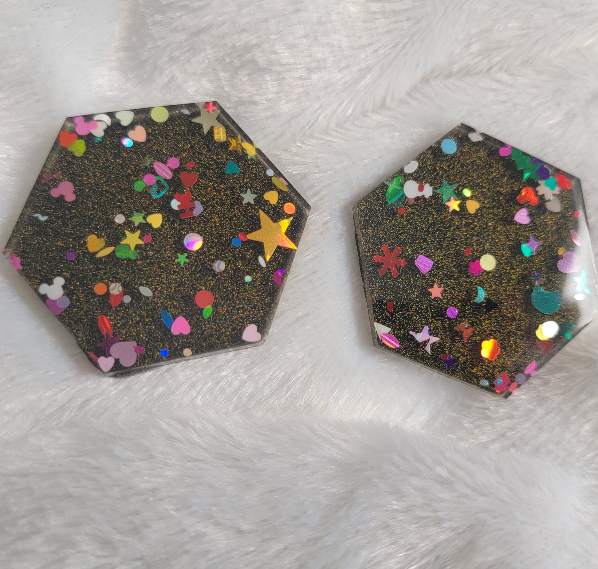 Two hexagon shaped epoxy resin pieces filled with assorted glitter shapes and a gold holographic base.