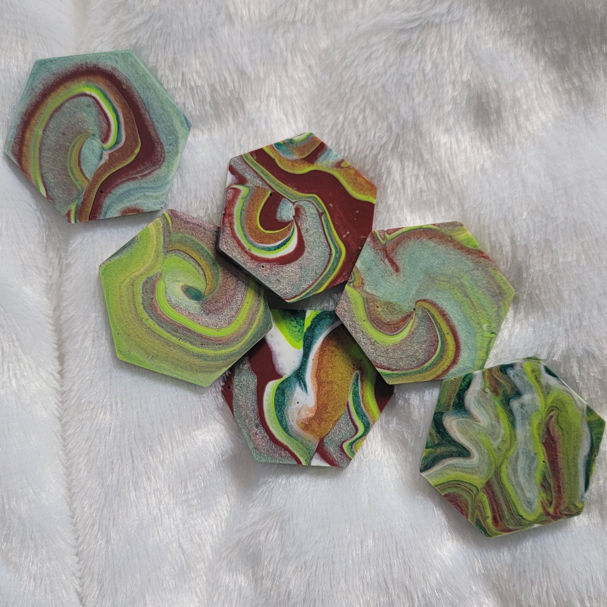 Hexagon shaped epoxy resin pieces with swirling greens and rust colored pigments, displayed on a white background.