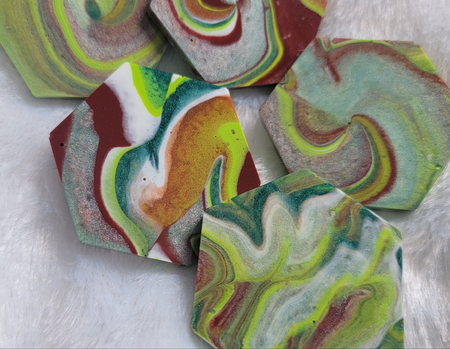 Hexagon shaped epoxy resin pieces with swirling greens and rust colored pigments, displayed on a white background.