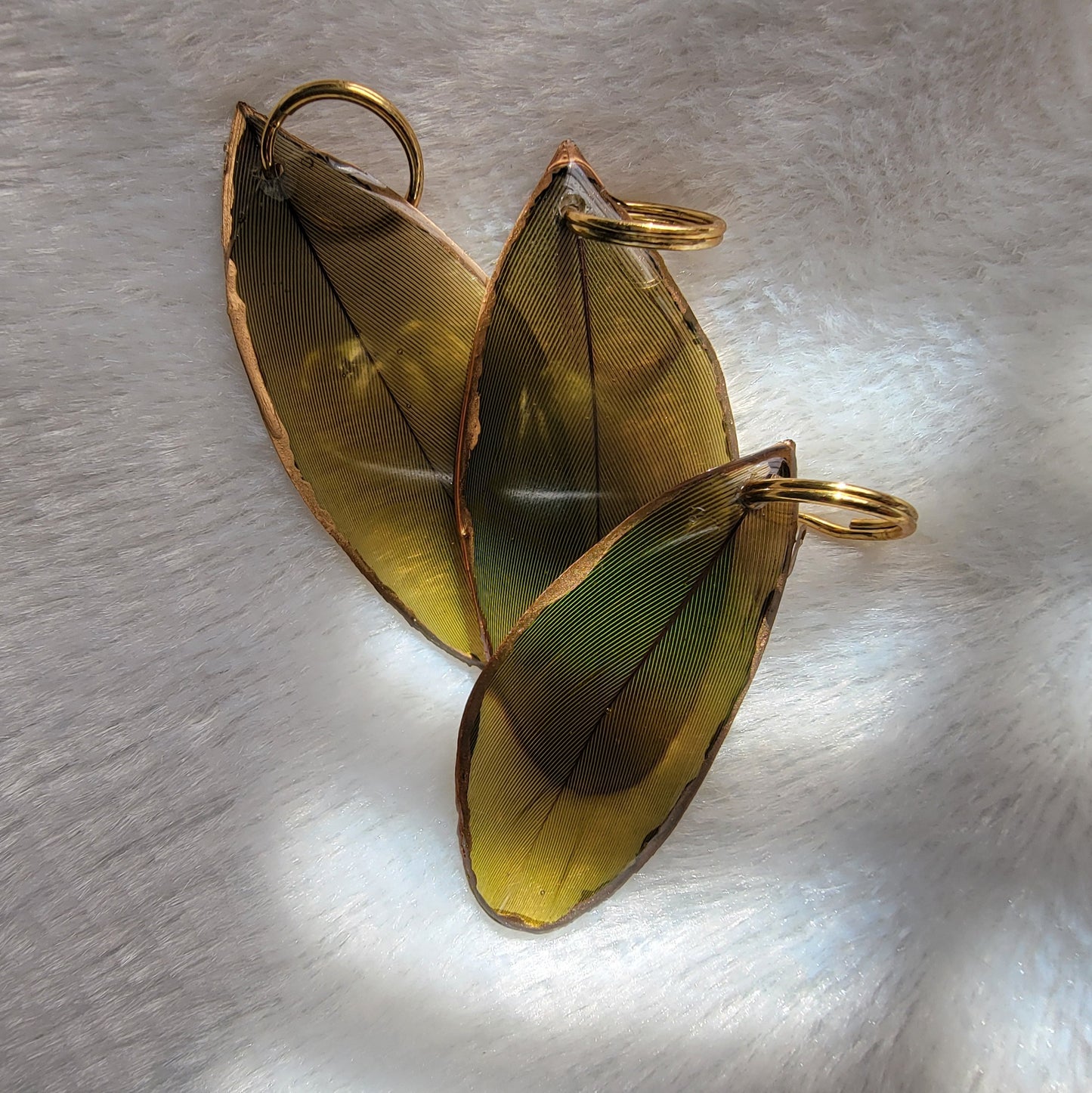 Three green feathers coated in epoxy resin, with gilded edges.