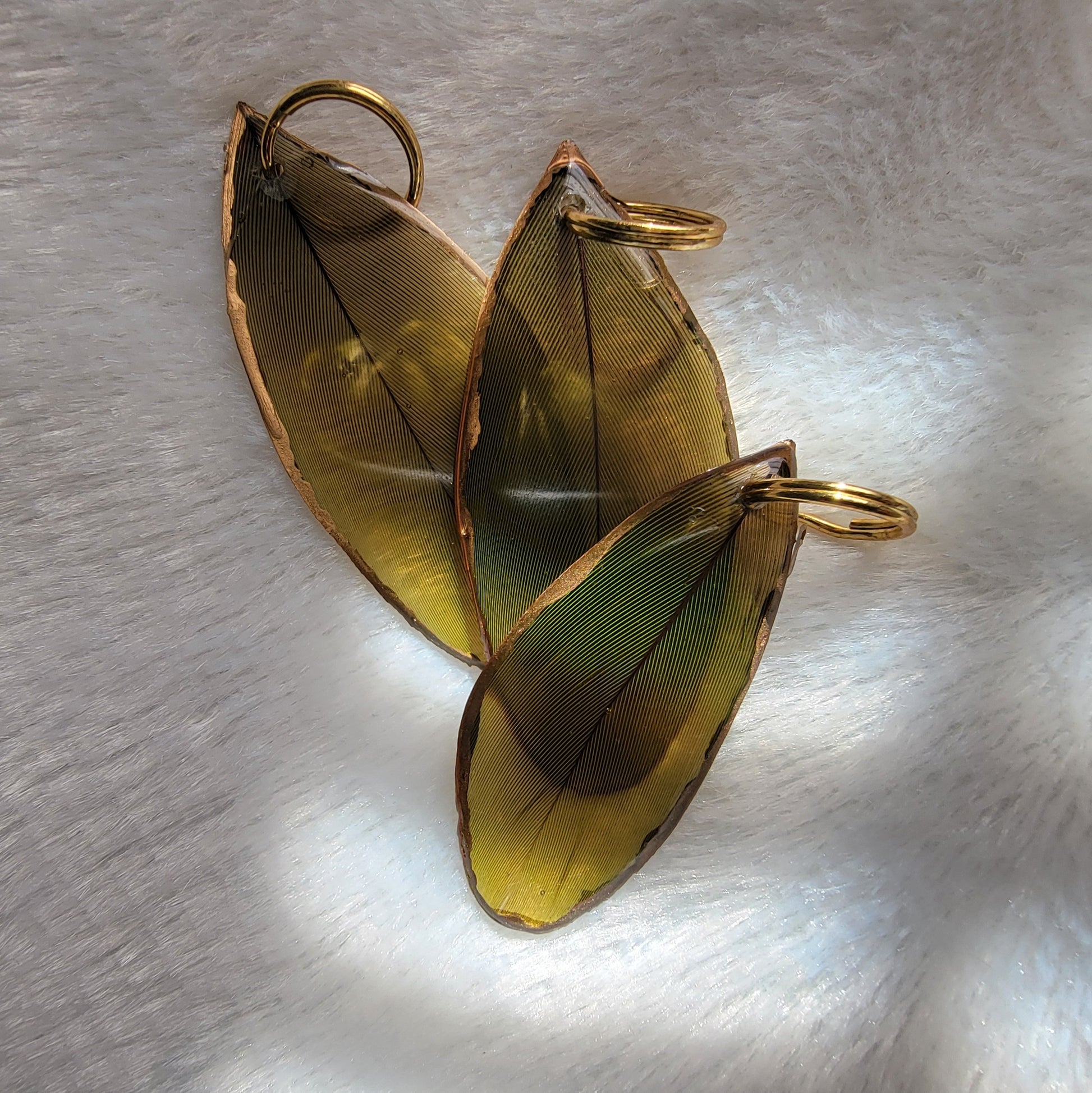 Three green feathers coated in epoxy resin, with gilded edges.