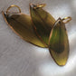 Three green feathers coated in epoxy resin, with gilded edges.