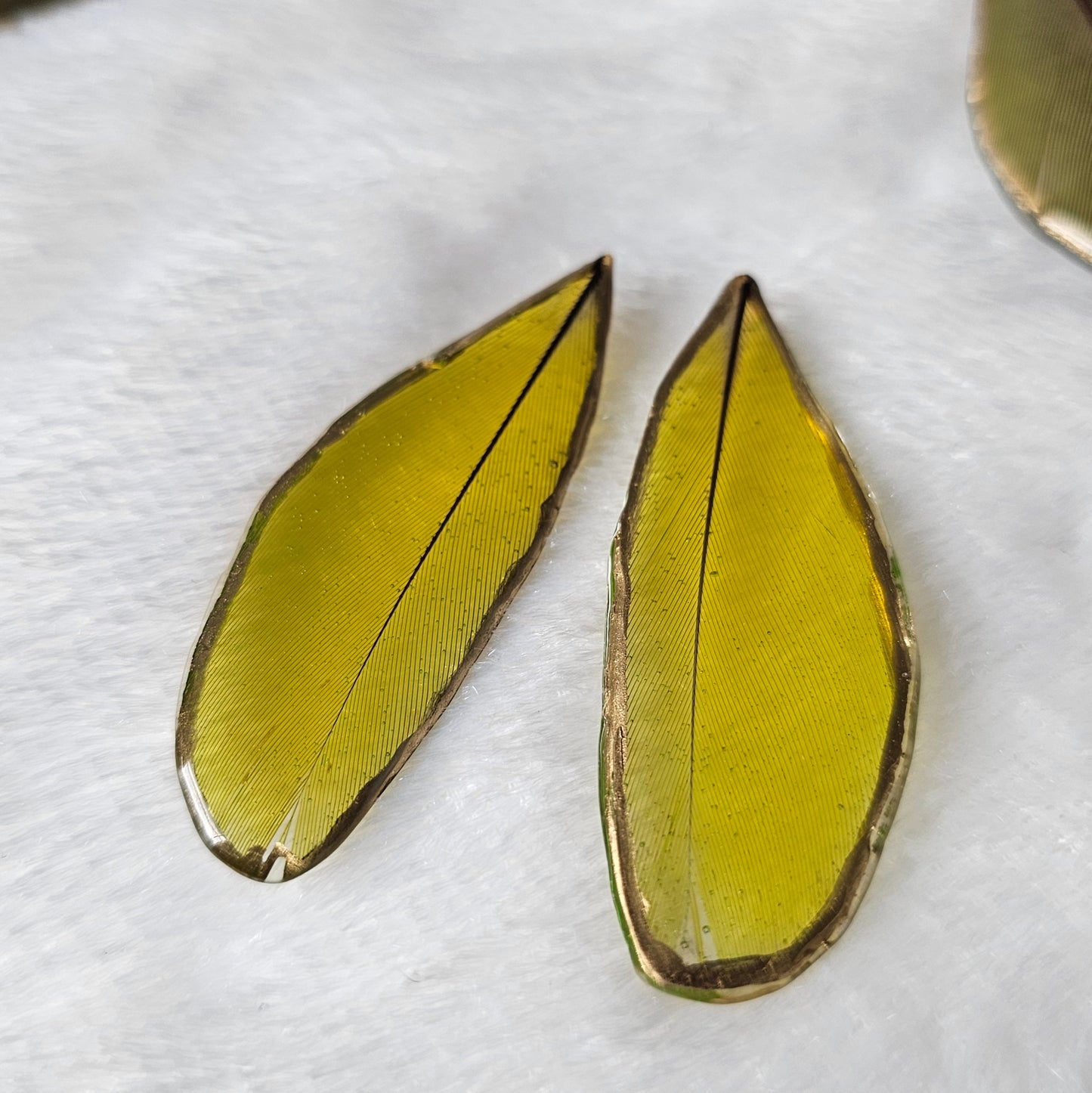 Bright green macaw feathers with gilded edges and sealed in epoxy resin, displayed on a white background.