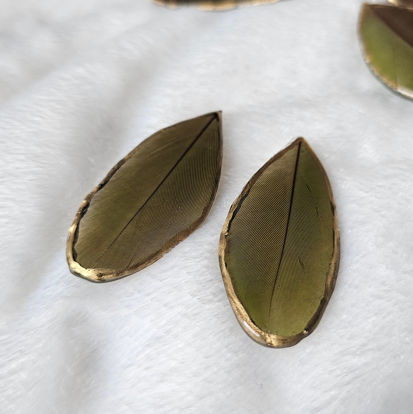 Green macaw feathers with gilded edges and sealed in epoxy resin, displayed on a white background.
