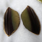 Green and dark brown macaw feathers with gilded edges and sealed in epoxy resin, displayed on a white background.