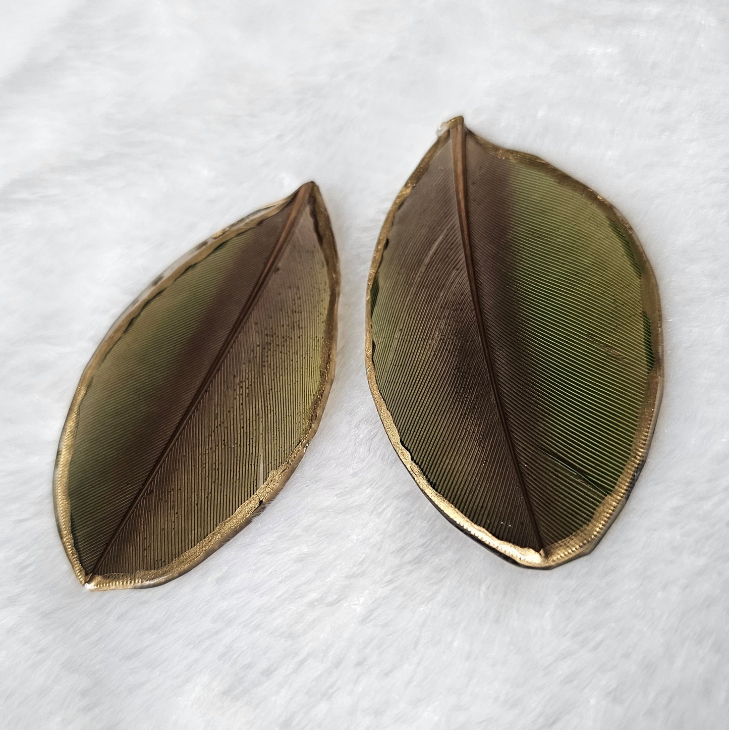 Green and dark brown macaw feathers with gilded edges and sealed in epoxy resin, displayed on a white background.