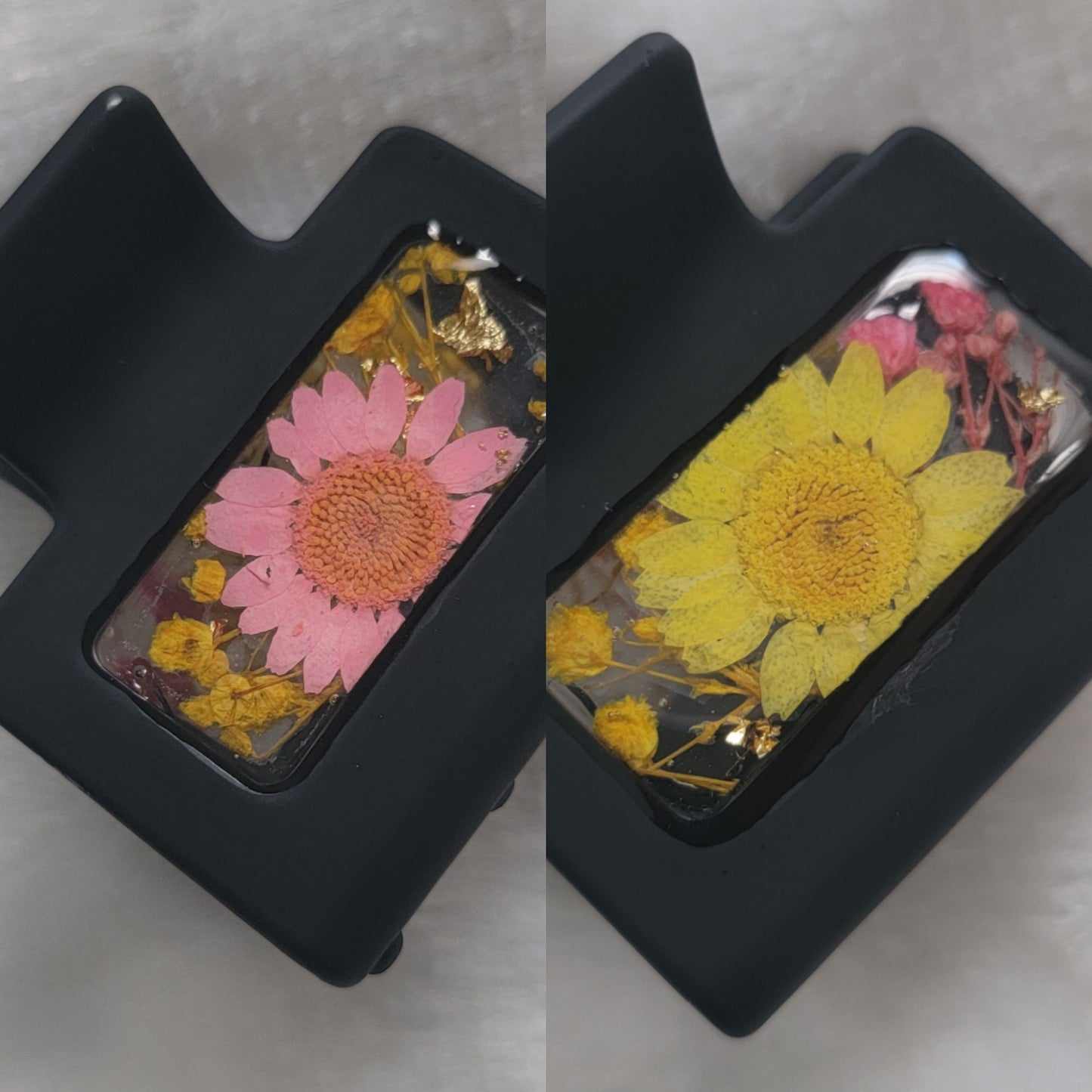 A black 2-inch claw clip with pink and yellow pressed flowers cast in resin within an open space in the hair clip. 
