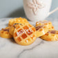 Several waffle shaped resin pieces sitting on marble table in front of a coffee mug, one has the name "Maple".