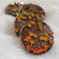 Four round epoxy resin pieces with dark brown glitter and holographic orange fall leaf shaped glitter.