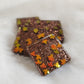 Four square epoxy resin pieces with dark brown glitter and holographic orange fall leaf shaped glitter.