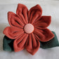 Fabric flower made with cotton corduroy, warm rusty red petals with a dusty pink center and two deep muted green leaves.