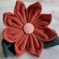 Fabric flower made with cotton corduroy, warm rusty red petals with a dusty pink center and two deep muted green leaves.