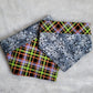 Two reversible Halloween pet bandanas, one side has greyscale tree branches and bats print while the other side is black and neon plaid.