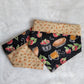 Two reversible pet bandanas, one side is light tan with orange and green fall leaves and the other side black with apples and apple treats like pies and cider.