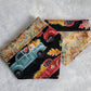Two reversible pet bandanas, one side has print of woods in the fall and the other has trucks with pumpkins.