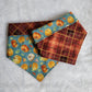Two reversible pet bandanas, one side has pumpkins on dusty blue background and the other side is dark rusty brown and gold plaid.