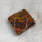 Square epoxy resin piece with fall trees scene made of copper and silver colored jewelry wire and holographic orange leaf shaped glitter.