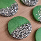 Round epoxy resin pieces, each one made half-and-half with sage green pigment and bright silver glitter.