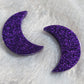 Two crescent moon shaped epoxy resin pieces made with deep purple glitter.