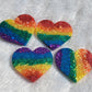 Four heart shaped epoxy resin pieces, each with glittery rainbow stripes.