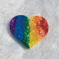Heart shaped epoxy resin piece with glittery rainbow vertical stripes.