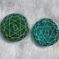 Two round epoxy resin pieces made with sparkling green glitter and pigment, each has heart chakra symbol made with vinyl - one golden one opal white.