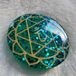 Round epoxy resin piece made with sparkling green glitter and pigment, has heart chakra symbol made with golden vinyl.